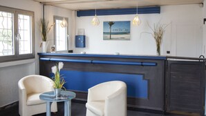 A reception area with a blue counter, two white armchairs, a glass table with a vase, and a framed picture on the wall. - Bel Azur (Six-Fours-les-Plages)