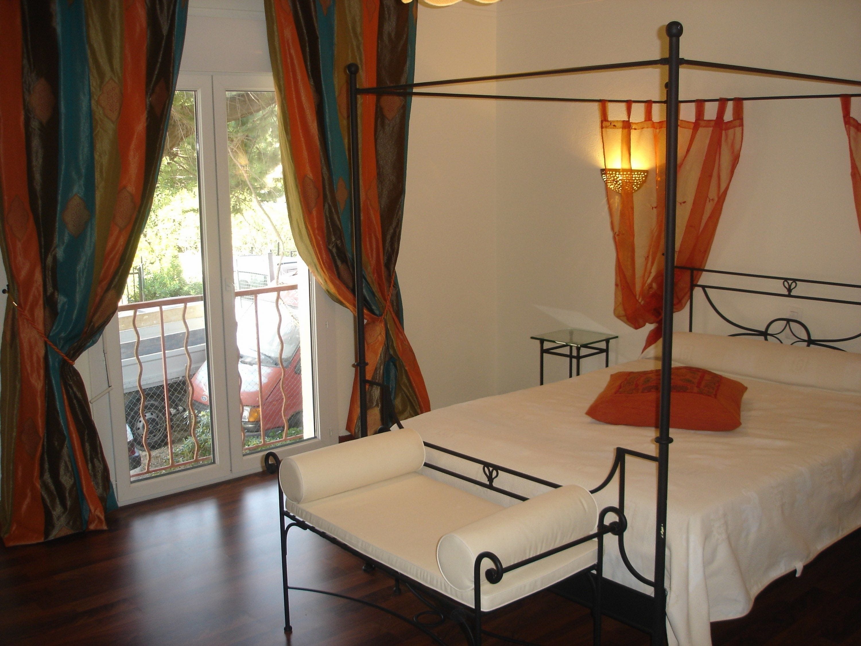Una cama con dosel con un colchón blanco y una sola almohada naranja. Junto a la cama hay una pequeña mesa de vidrio.