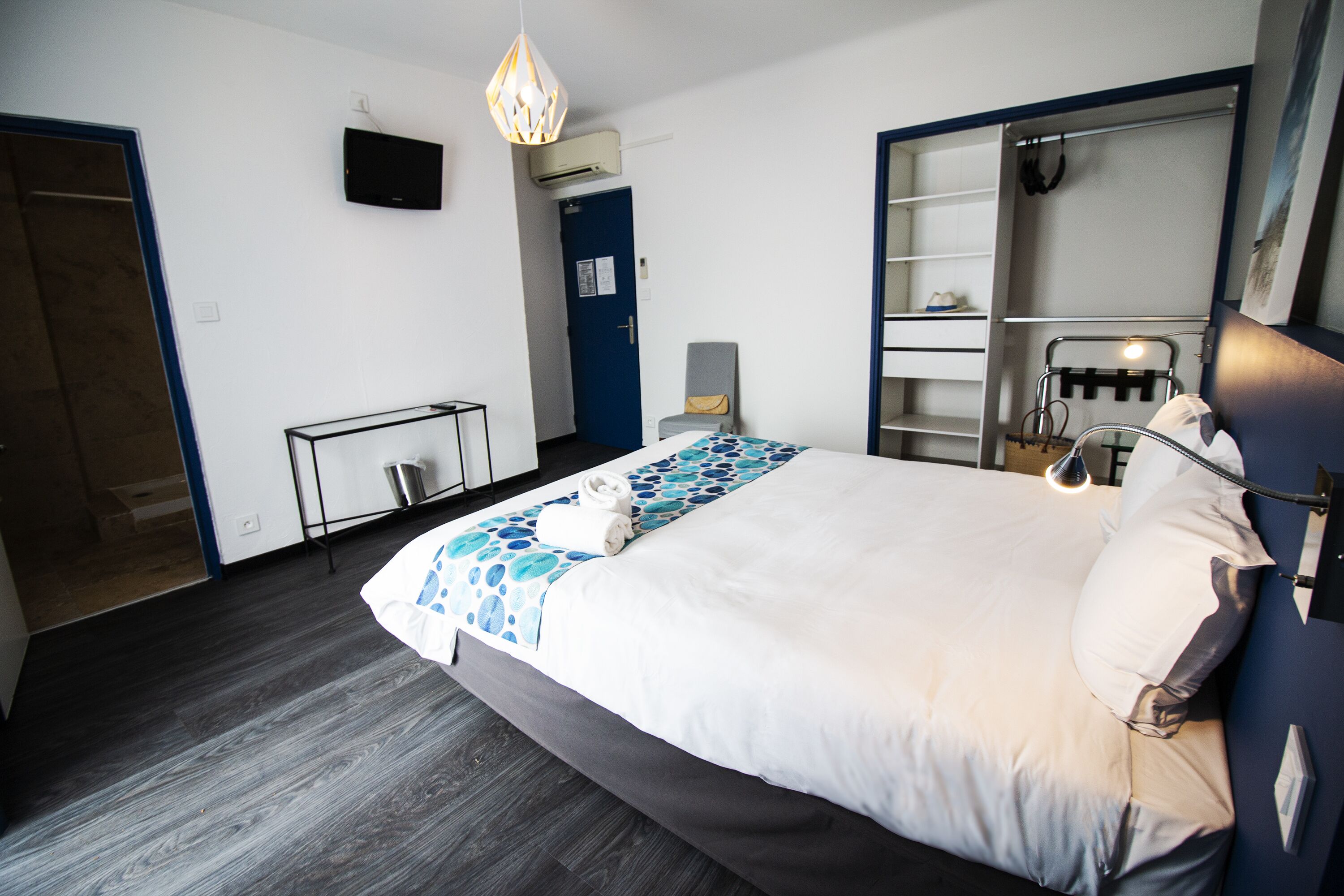 Una camera d'albergo moderna con un letto grande, una scrivania, una sedia, un armadio e un televisore appeso al muro.