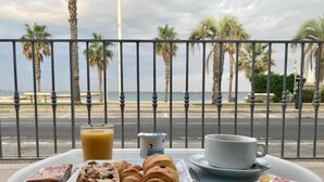 A breakfast tray with pastries, a glass of orange juice, a cup, and a plate of food on a balcony overlooking a beach with palm trees and the ocean. - Bel Azur (Six-Fours-les-Plages)