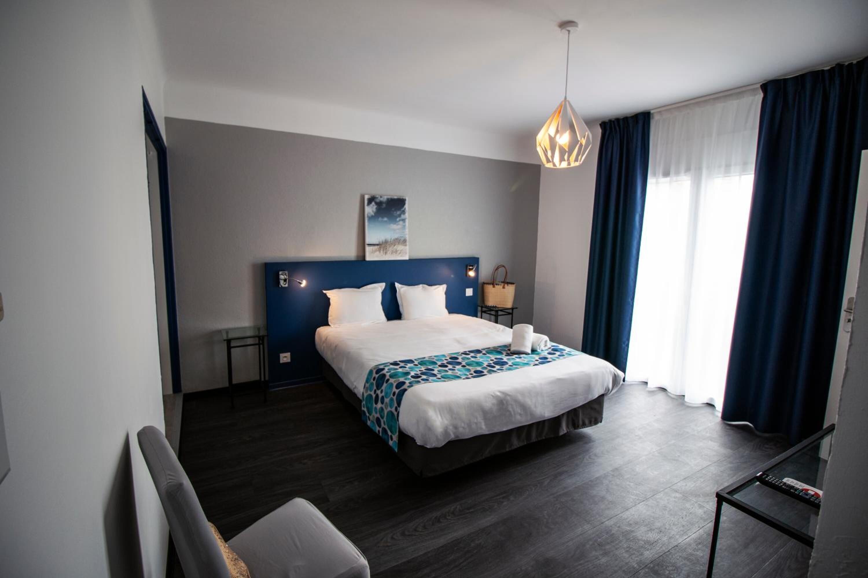 Une chambre d’hôtel moderne, dotée d’un grand lit, d’une table de chevet, d’une chaise, d’un bureau et d’une fenêtre avec des rideaux.