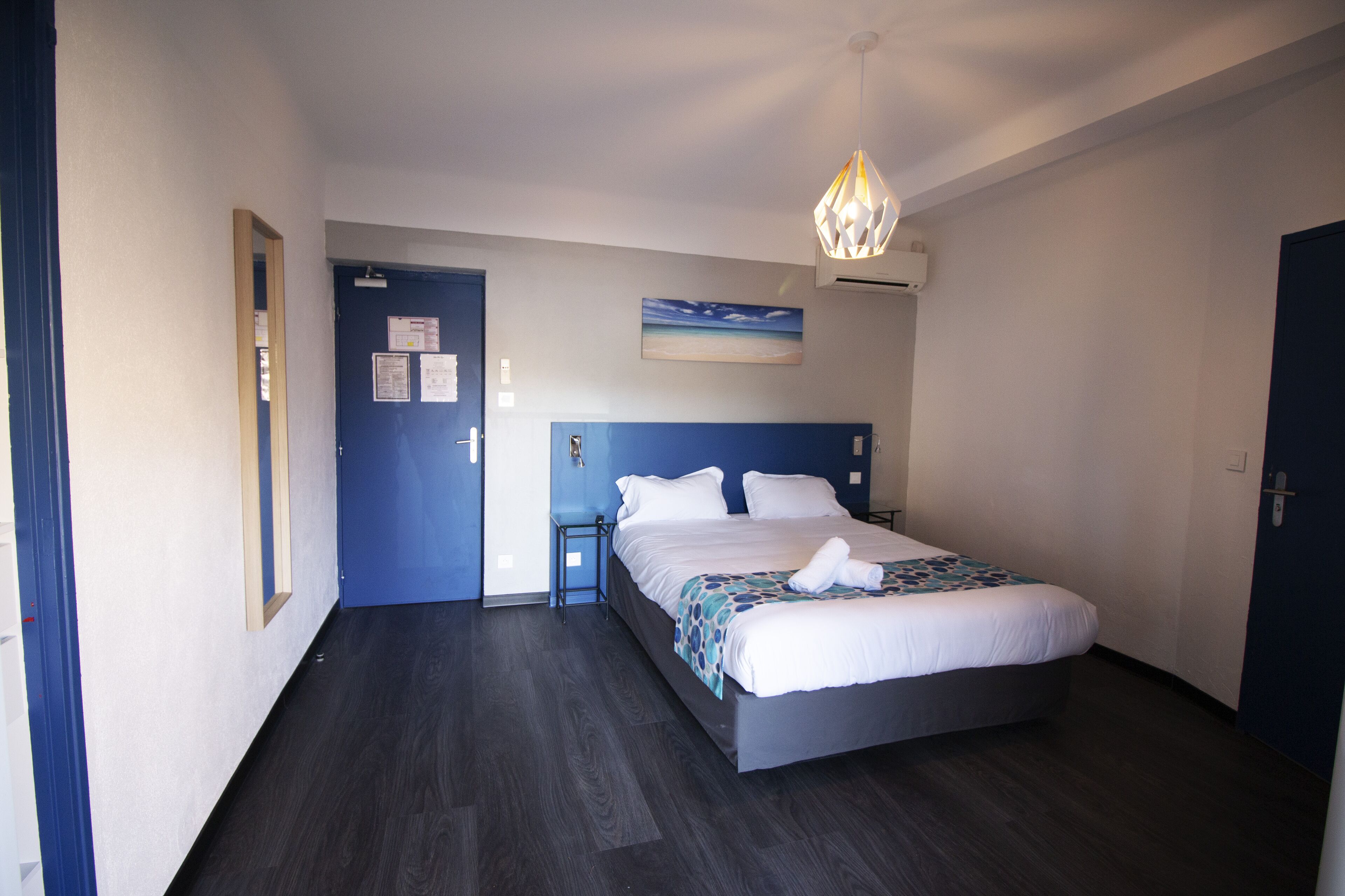 A bedroom with a bed, a bedside table, a nightstand, a wall-mounted air conditioner, and a ceiling light fixture.