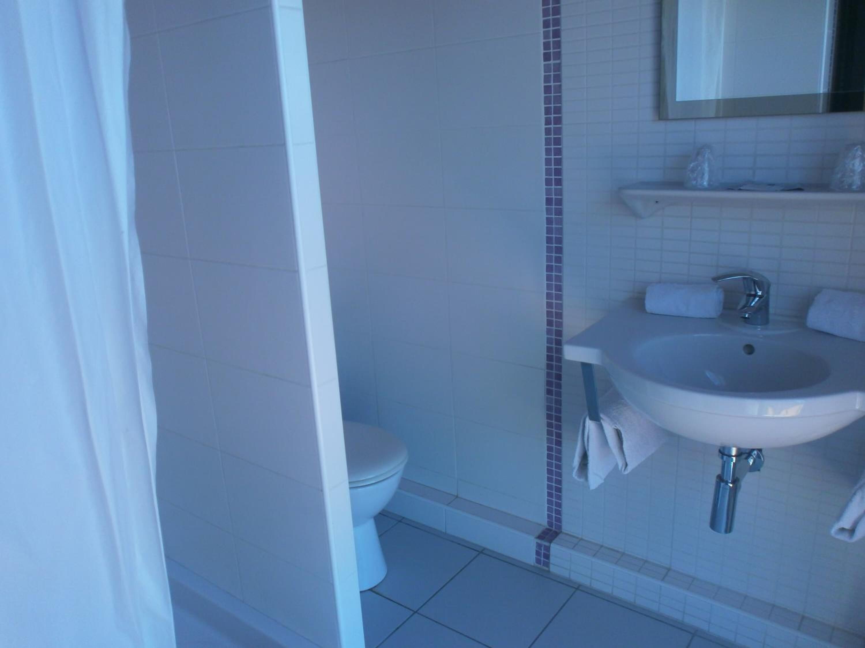 Une salle de bain avec un lavabo blanc, des toilettes et un rideau de douche.
