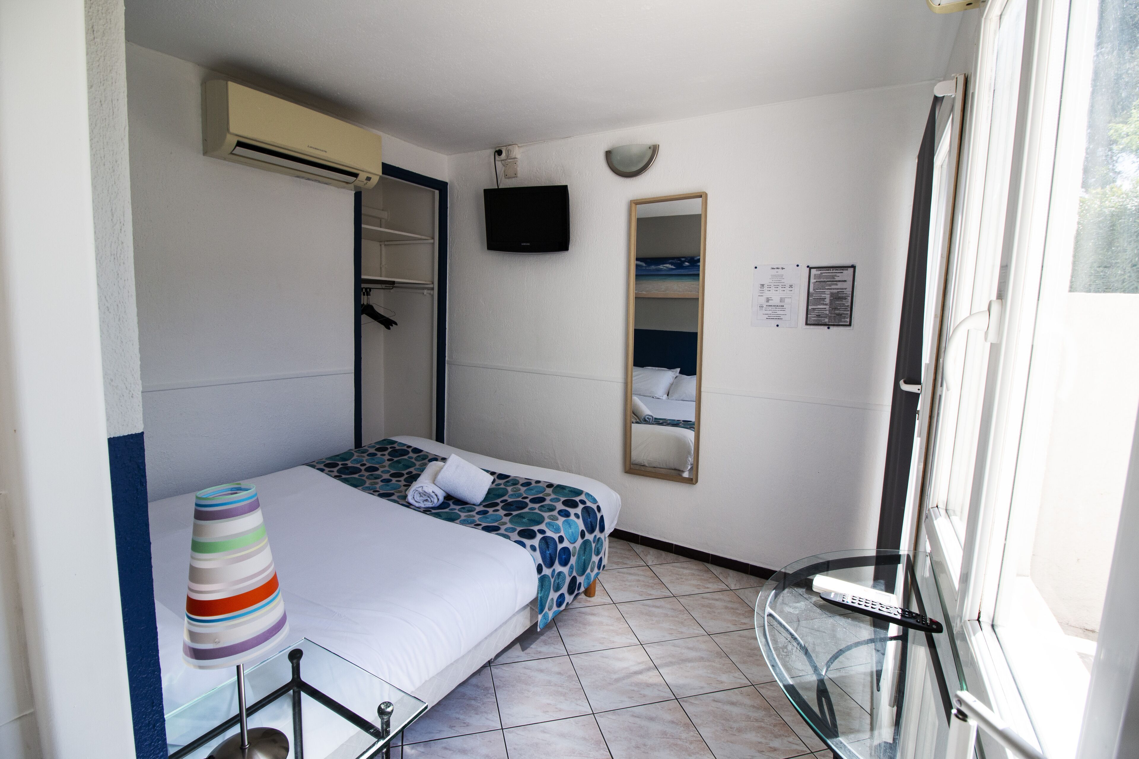 A hotel room with a bed, a glass table, a laptop, a TV, and a window.