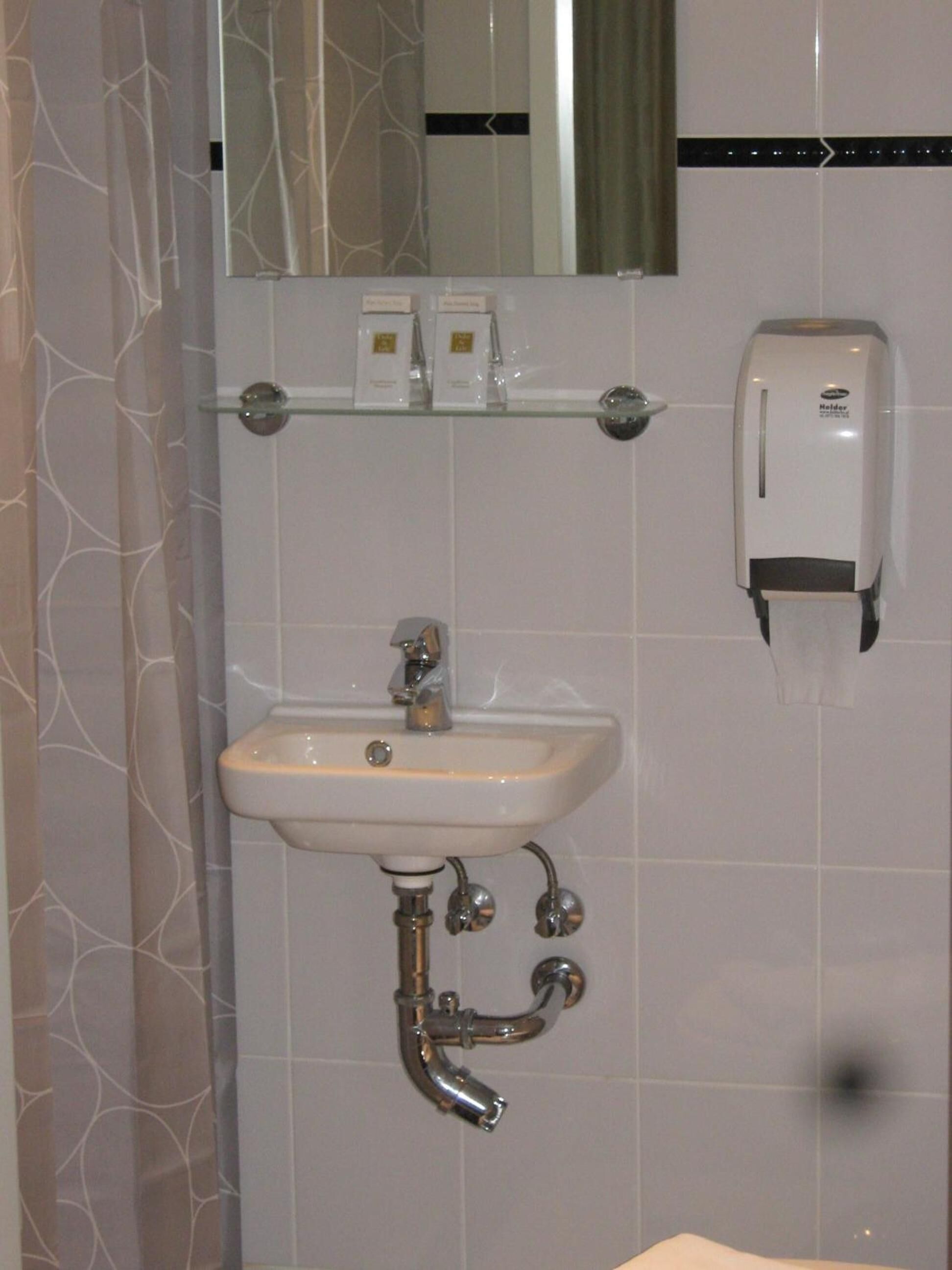Un baño con un lavamanos blanco, un espejo encima y un dispensador de jabón en la pared.