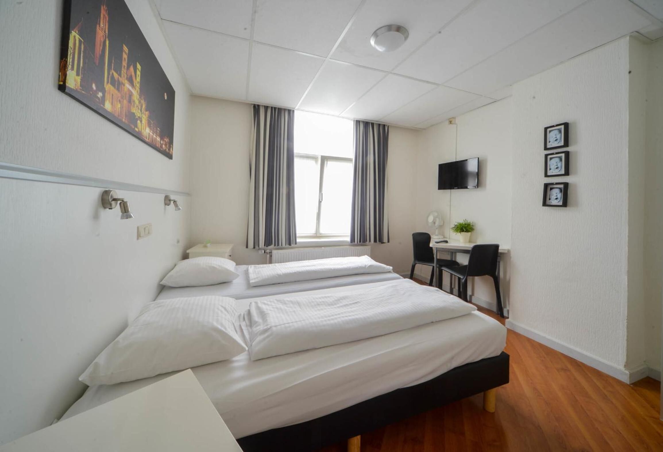 Une chambre d’hôtel avec deux lits, un bureau, une chaise, une télévision et une fenêtre avec des rideaux.