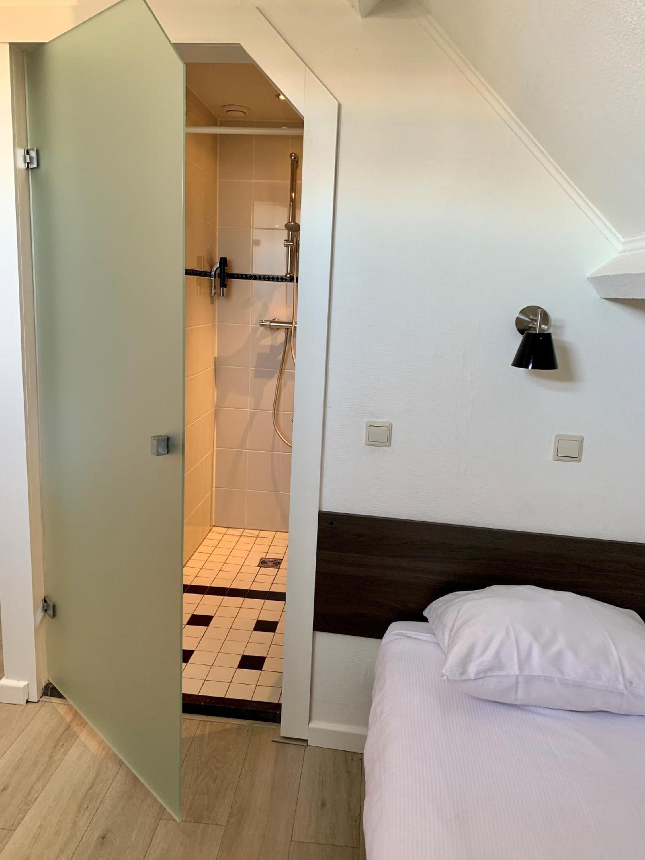 Een hotelkamer met een bed, een douchegedeelte en een wandlamp.