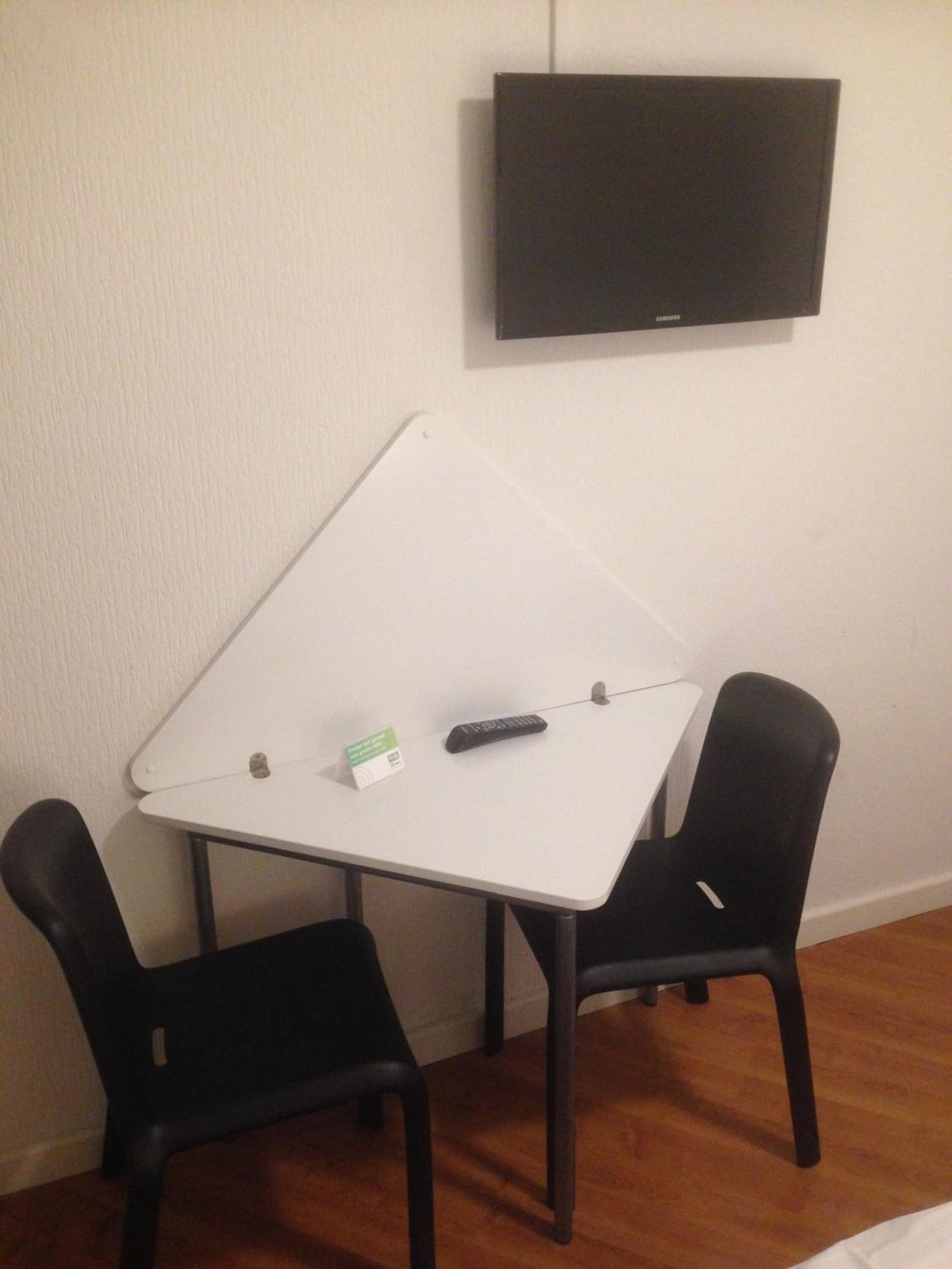 A small room with a white table, two black chairs, a remote control, and a television on the wall.