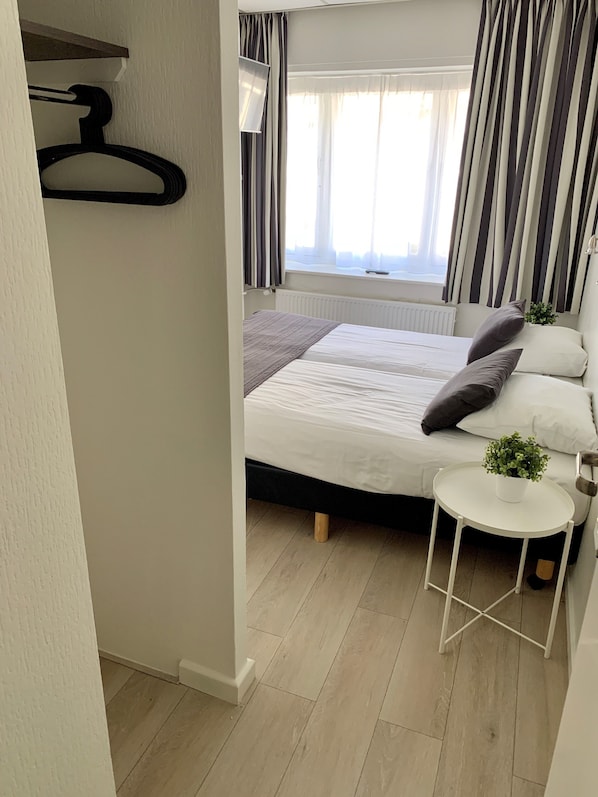 Un dormitorio ordenado con cama, mesita de noche y perchero.
