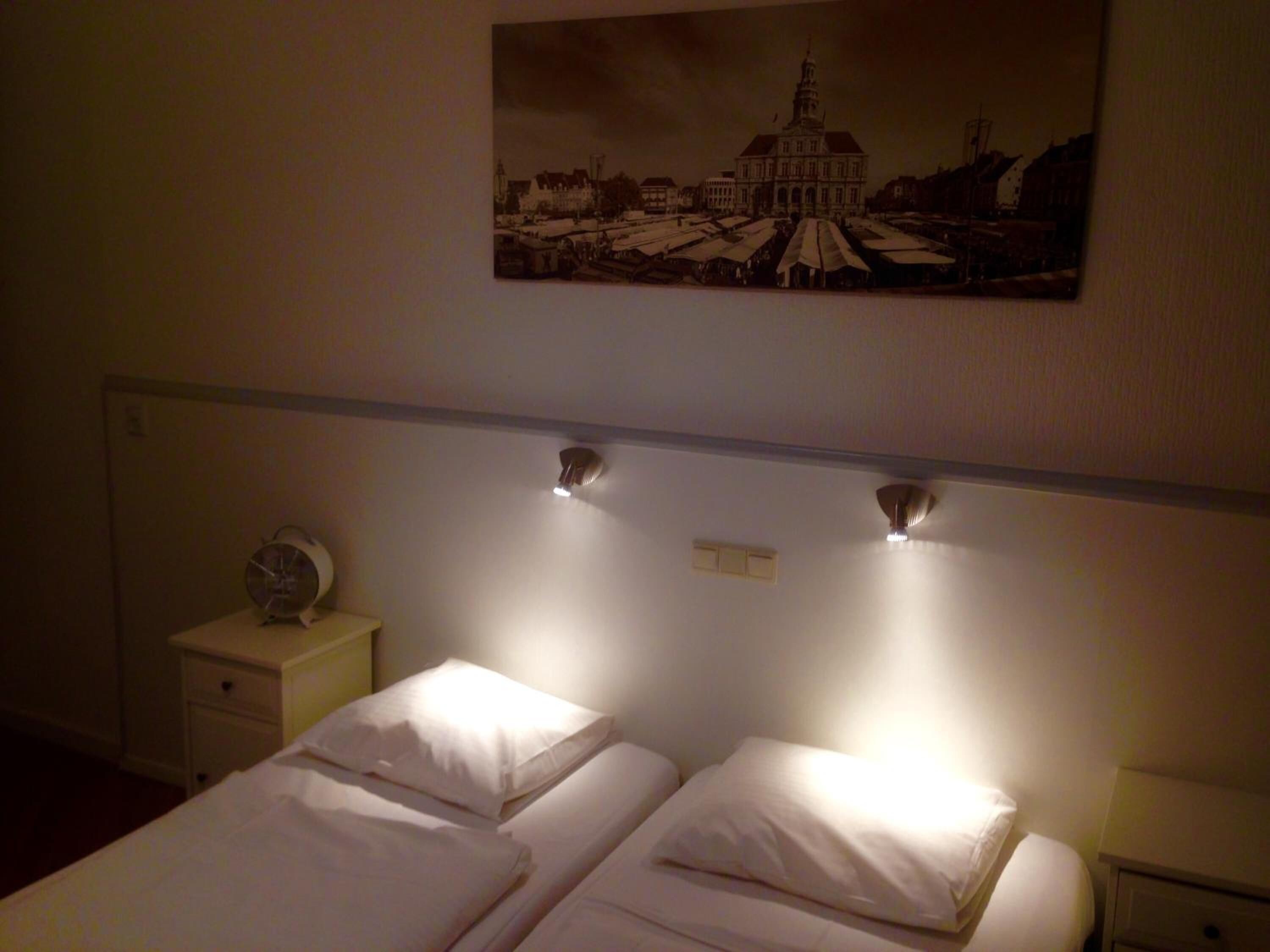 Habitación de hotel con dos camas, una mesita de noche con un reloj y un cuadro de un edificio en la pared.