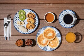 A breakfast setup with pancakes, kiwi slices, banana slices, and a cup of coffee on a wooden table.