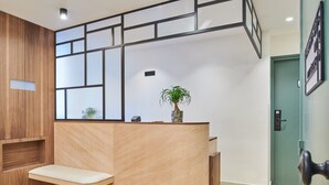 A reception desk with a wooden finish, a small plant on top, and a green door to the right. - Hotel 10 Opera by HappyCulture (Paris)