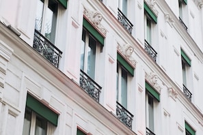 A building facade with multiple windows, green awnings, and decorative stone carvings.