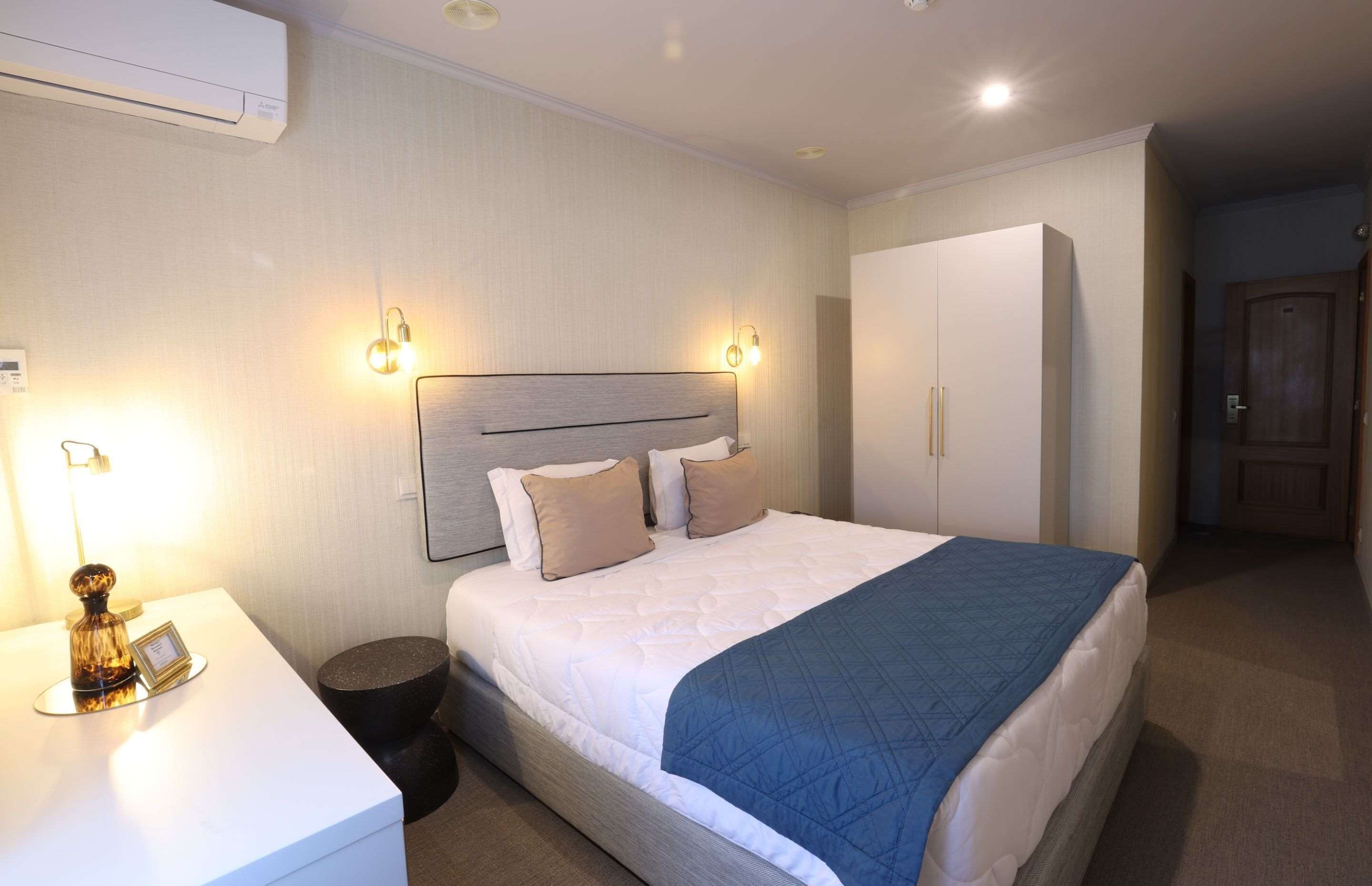 Una habitación de hotel con una cama grande, lámparas de noche, una mesita de noche y un armario.
