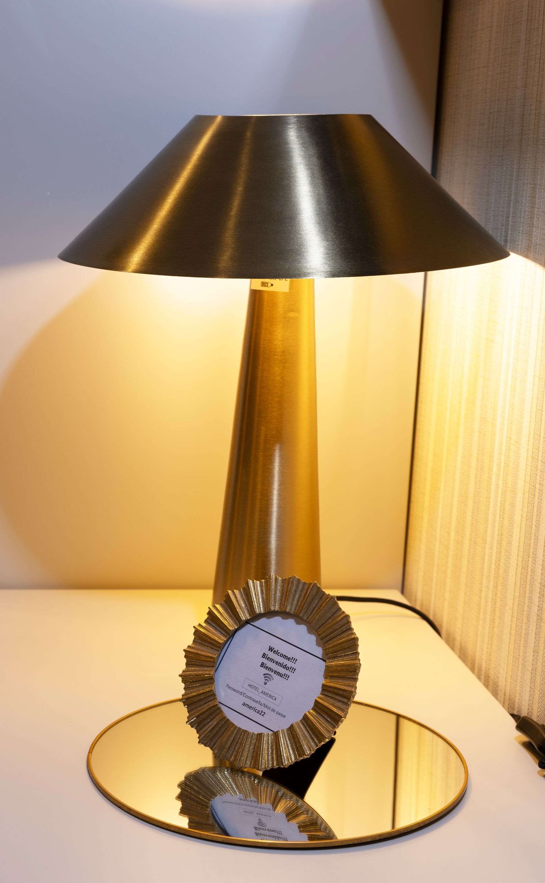 Une lampe de table avec un pied doré et un abat-jour noir, posée sur une surface blanche.
