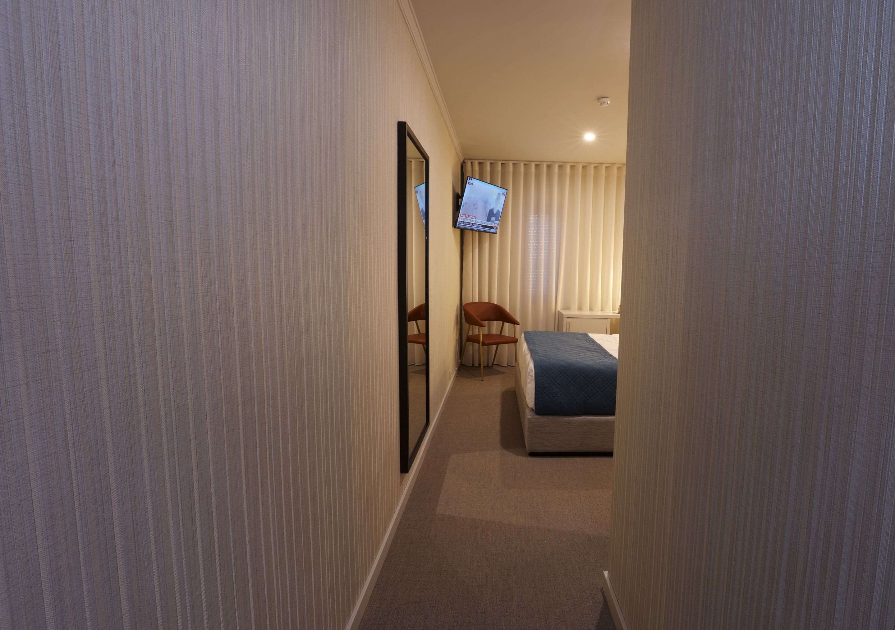Una habitación de hotel con una cama, un televisor montado en la pared, una silla y una mesita.