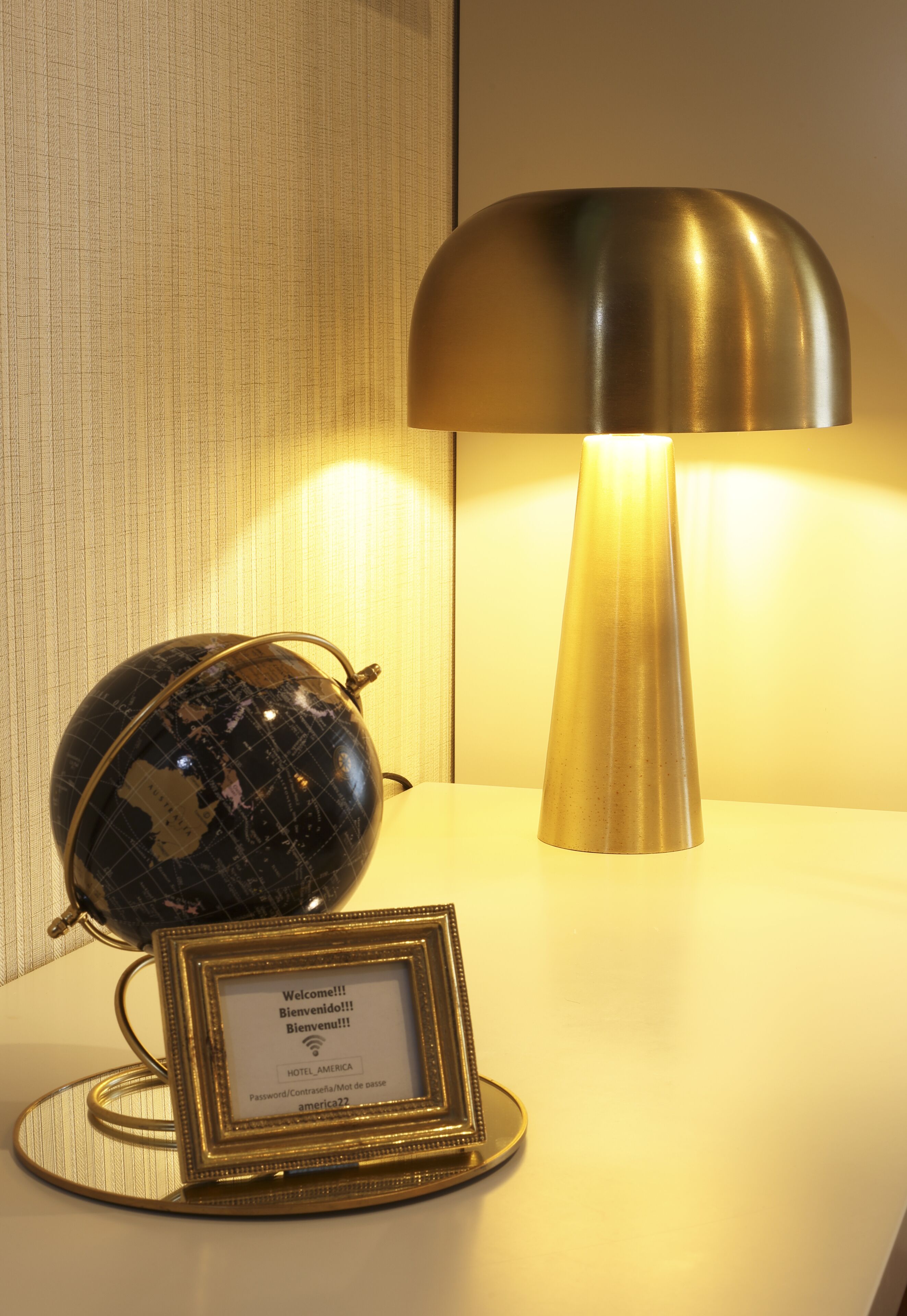 A globe and a framed welcome sign on a table with a lamp.
