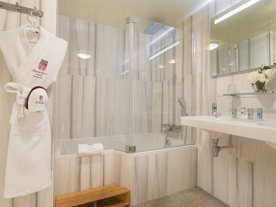 A modern bathroom with a glass-enclosed shower, a white sink with toiletries, and a robe hanging on a hook.