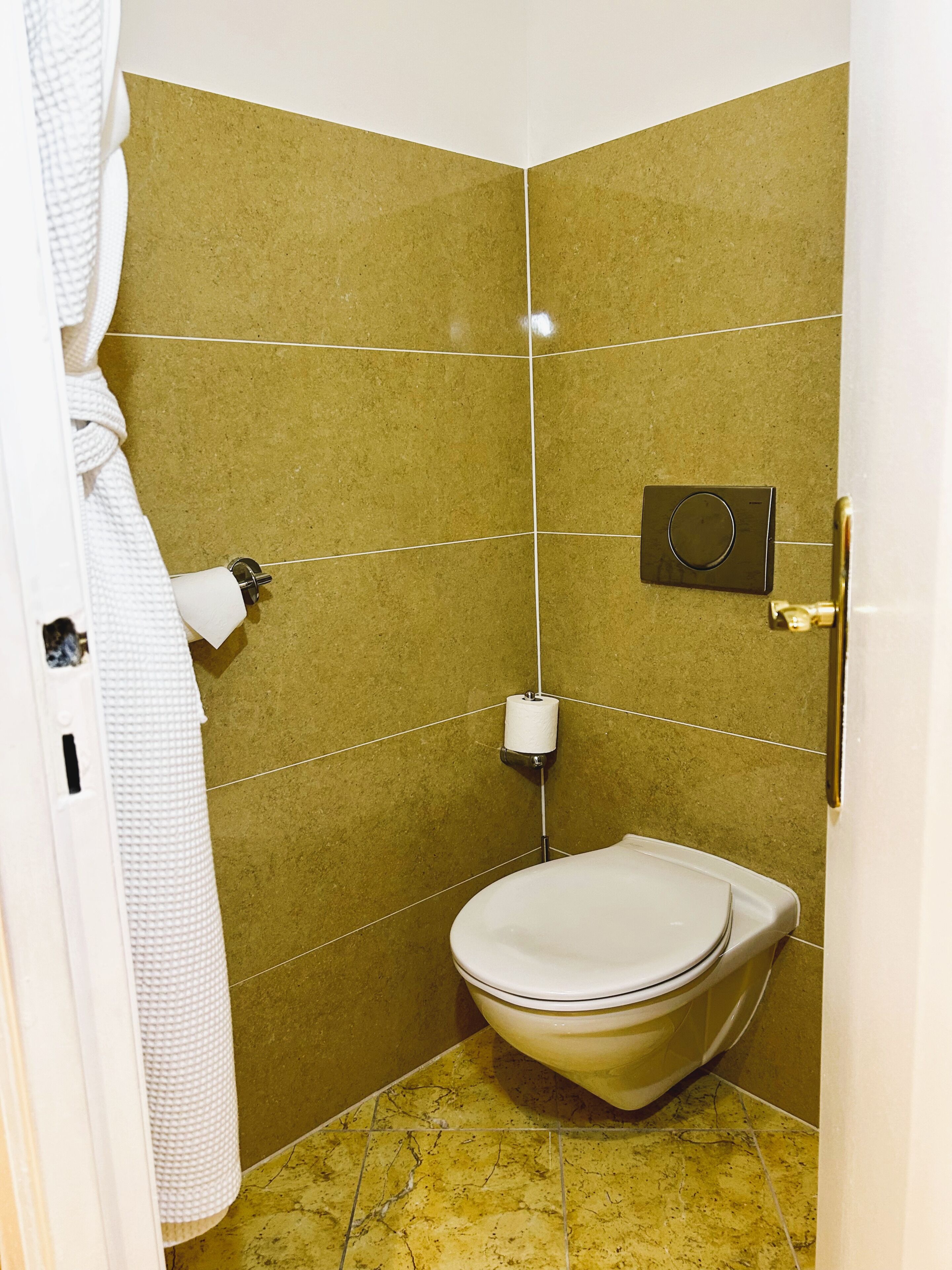 A small bathroom with a toilet, a towel dispenser, and a toilet paper holder on the wall.