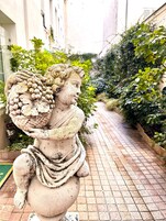 Una estatua de un ángel sosteniendo un racimo de uvas, ubicada en un camino pavimentado con vegetación a ambos lados.