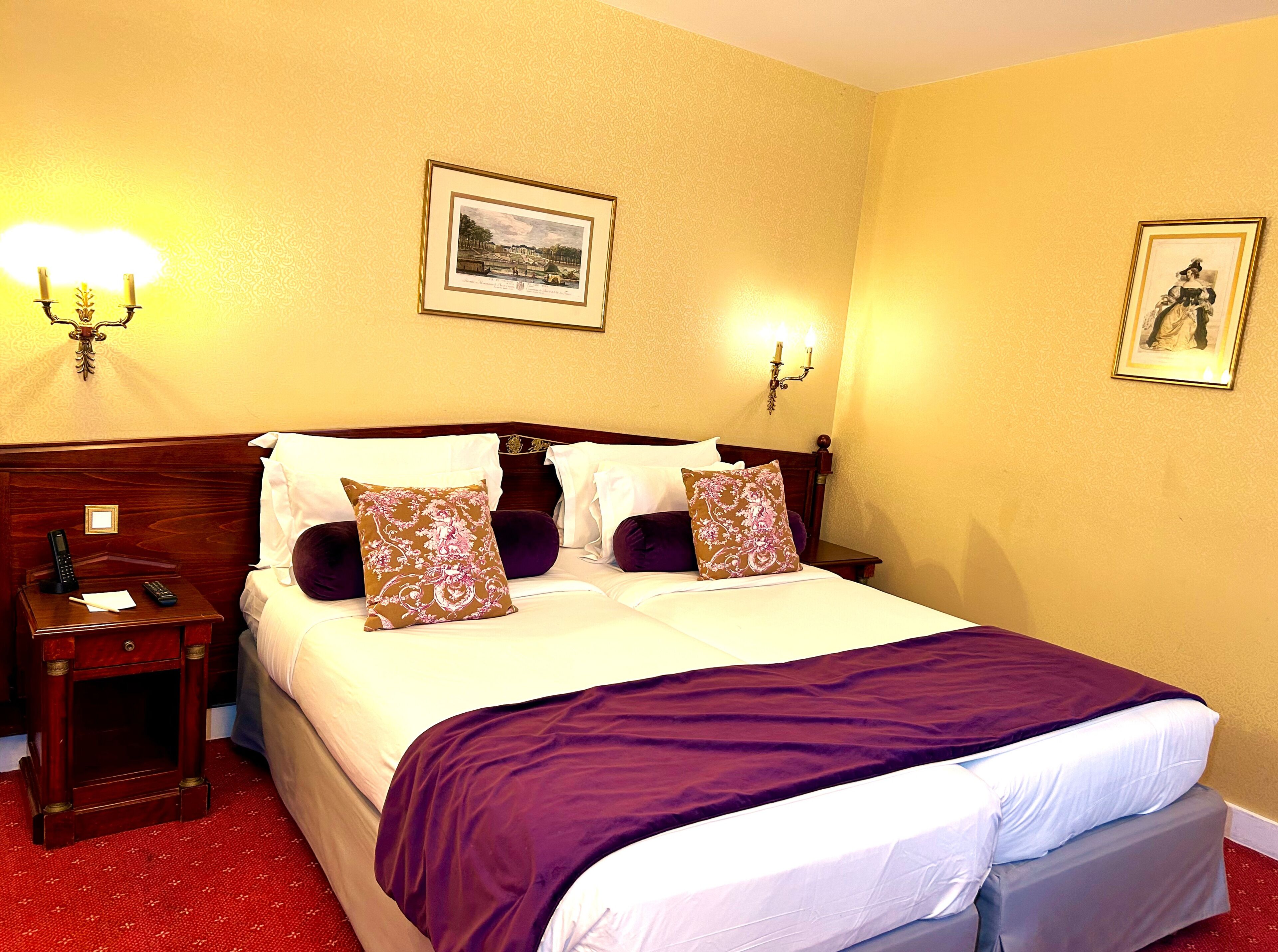 A neatly made bed with a purple blanket, two bedside tables with lamps, and framed pictures on the walls.