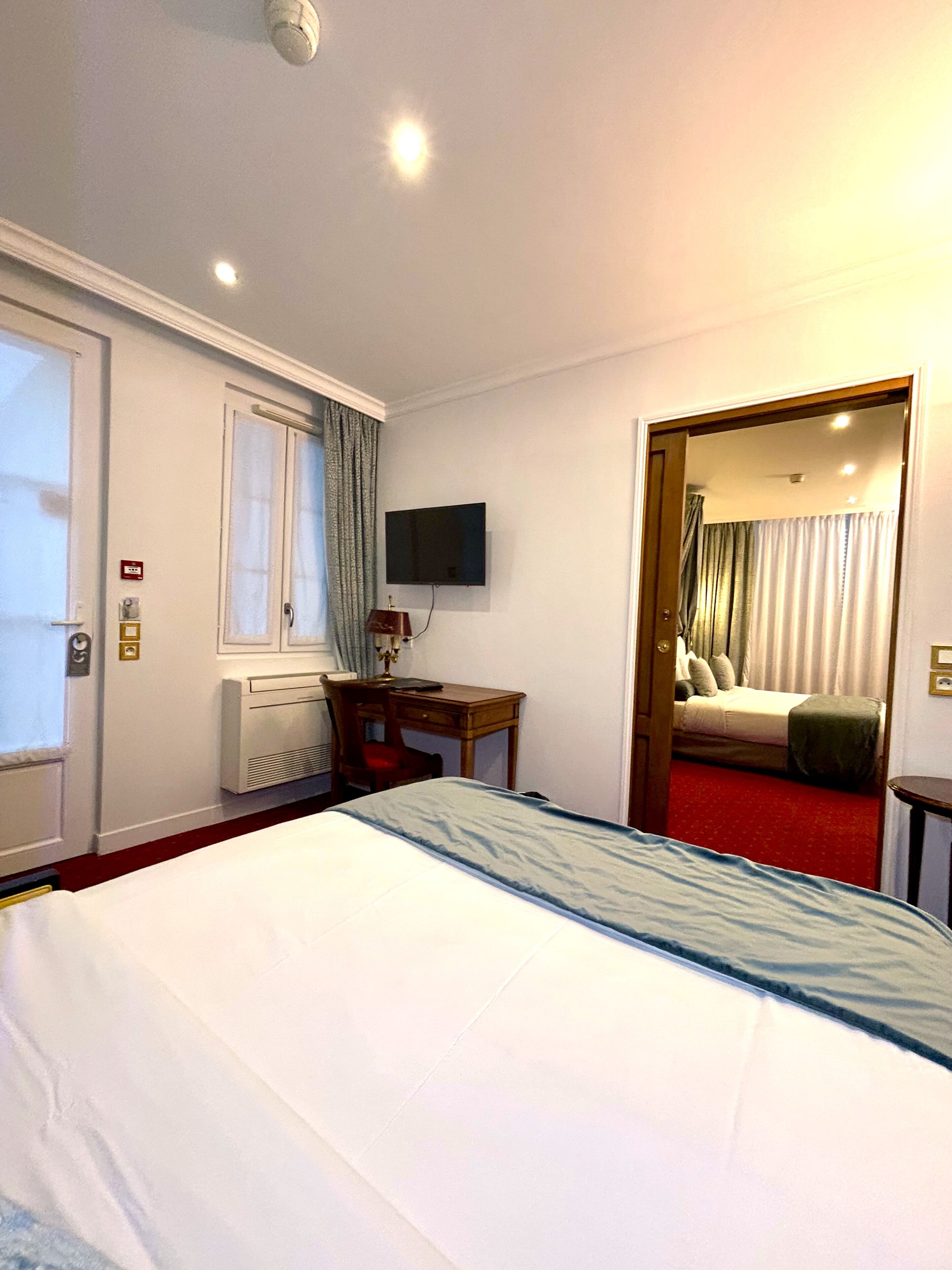 A hotel room with a bed, a desk, a chair, a television, and a door leading to a bathroom.