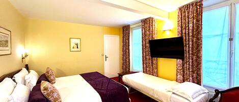 A hotel room with two beds, a TV, a red chair, a window with curtains, and a door.