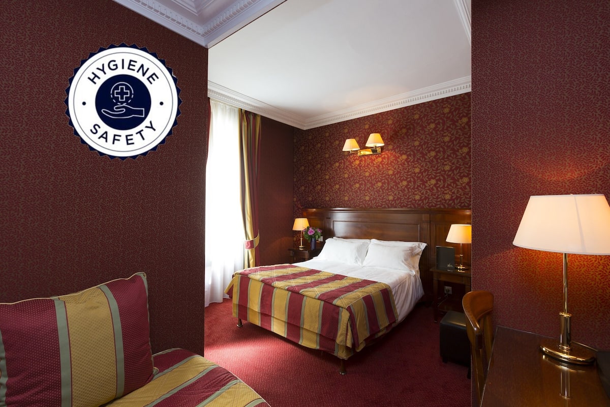 Una habitación de hotel con una cama, dos lámparas de noche, una mesita de noche, una silla y un escritorio.