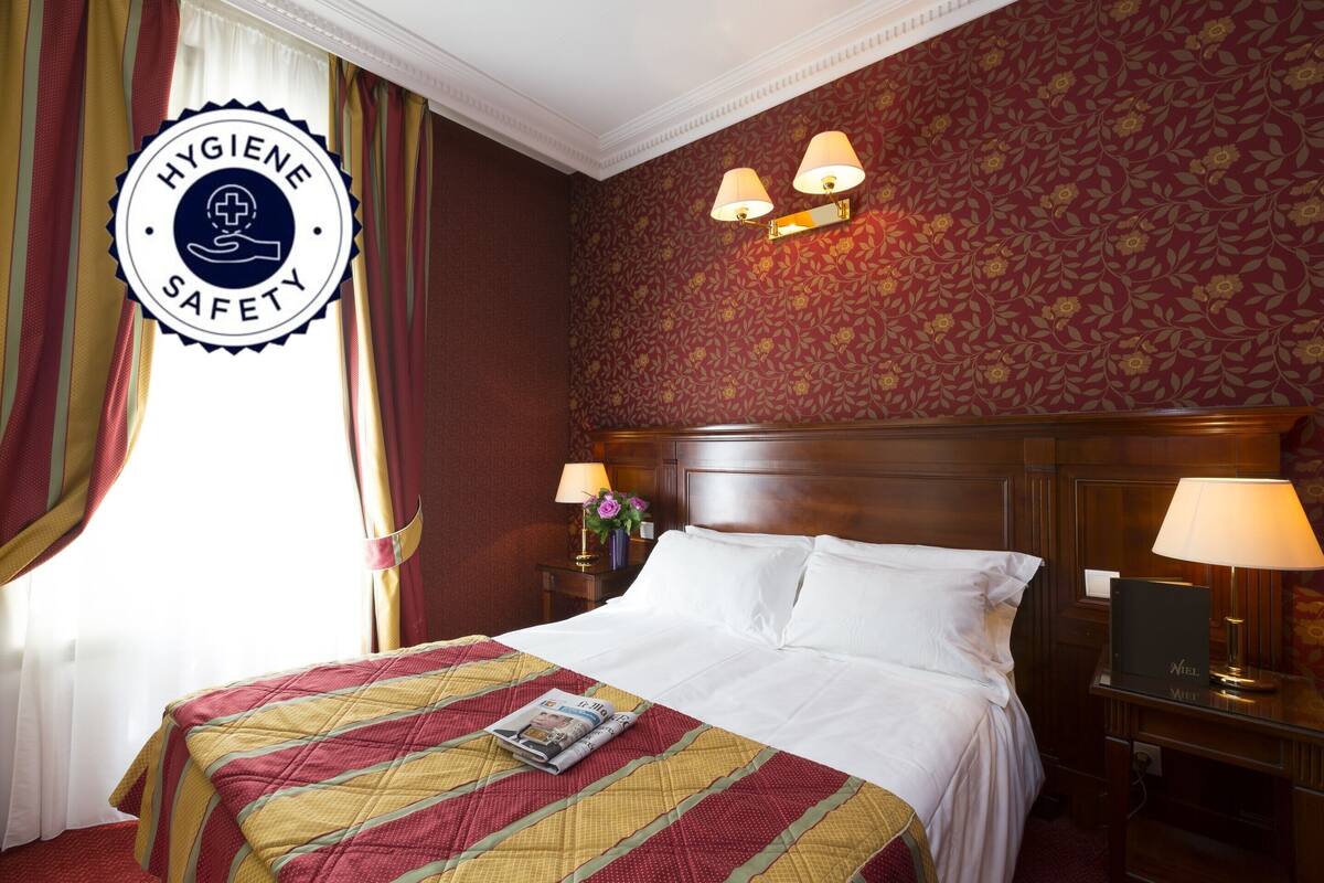 Una habitación de hotel con una cama grande, dos lámparas de noche, una mesita de noche y un papel tapiz floral.
