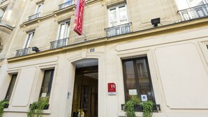 A hotel entrance with a red sign, a double door, and a small window with plants. - Hotel Niel (Paris)