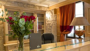 A reception desk with a glass top, a black leather chair, a vase with flowers, and a bookshelf filled with books. - Hotel Niel (Paris)