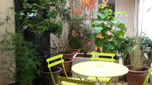 A small patio with a round table and two chairs, surrounded by potted plants and a green door. - Hotel Niel (Paris)