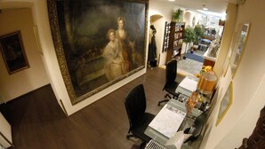 A room with a large classical painting, a desk with a computer, and a bookshelf. - Hotel Pension Excellence (Vienna)
