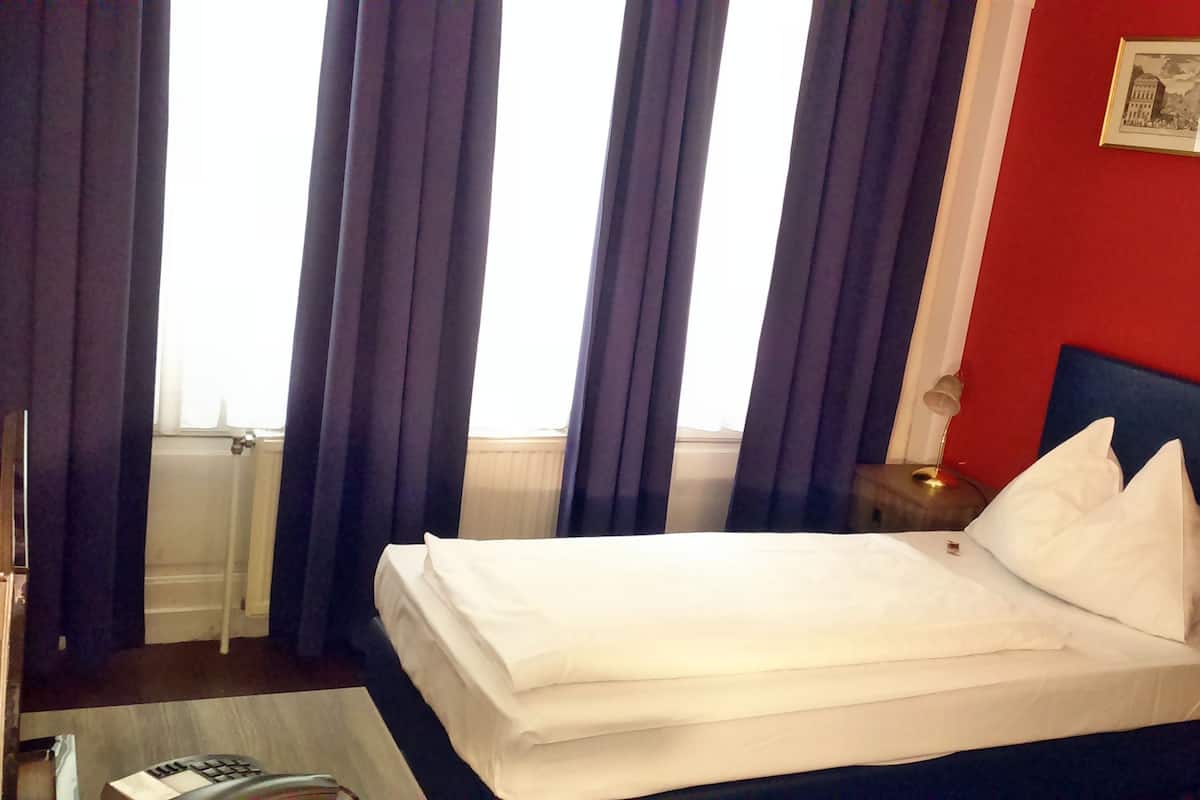 Hotellihuone, jossa on sänky, yöpöytä, lamppu ja seinällä oleva kehystetty kuva.
