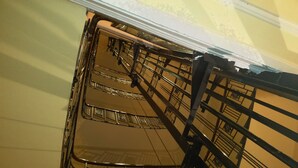 A spiral staircase with ornate metal railings and a mirrored wall reflecting the interior. - Hotel Pension Excellence (Vienna)