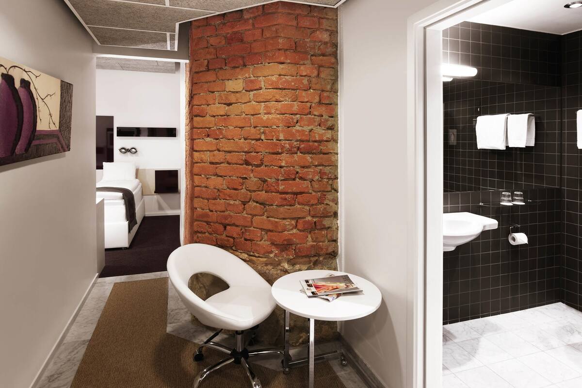 A modern bathroom with a black tiled wall, a white sink, and a small white table with a magazine.