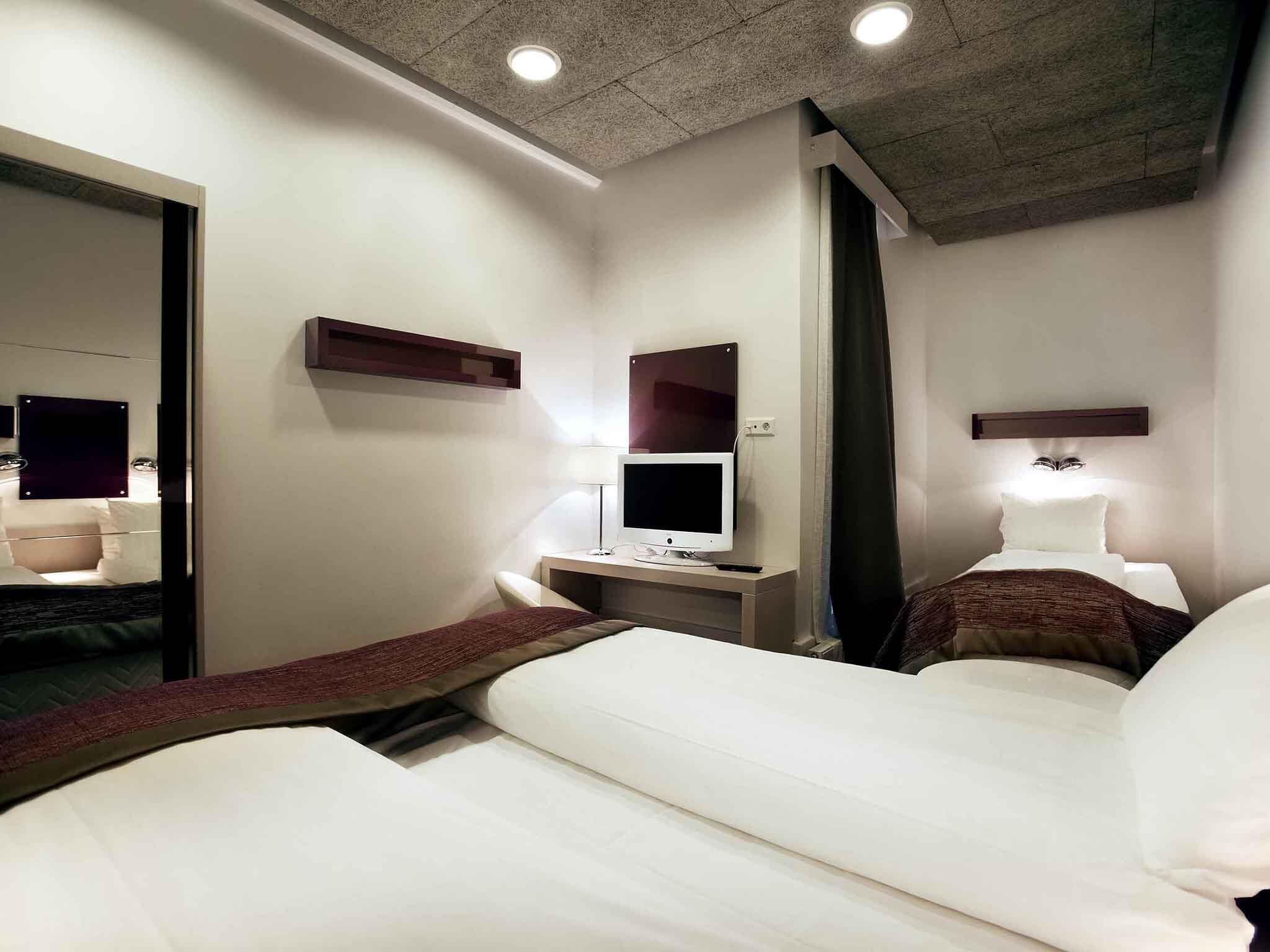 A hotel room with two beds, a desk with a computer, a mirror, and a ceiling light.