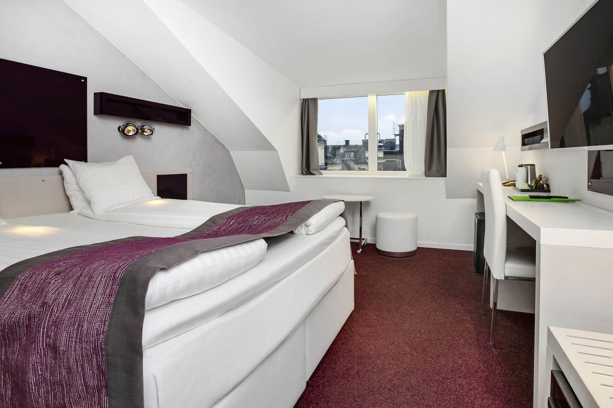 A modern hotel room with a bed, a desk, and a TV.