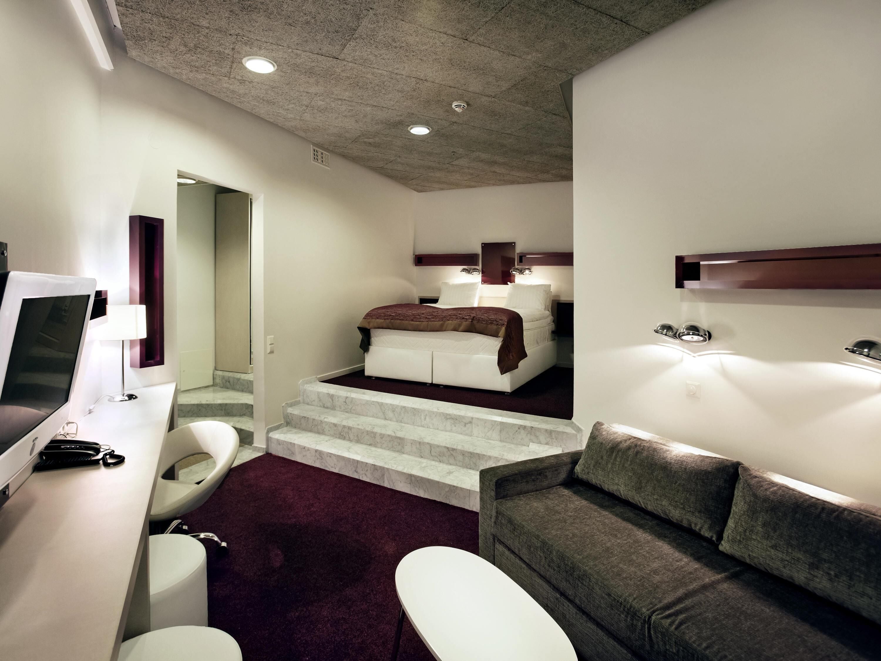 Una habitación de hotel moderna con cama, escritorio, silla, sofá y baño.