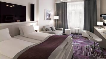 Een moderne hotelkamer met een groot bed, een bank, een bureau en een stoel. Er is een raam met gordijnen en een schilderij aan de muur.