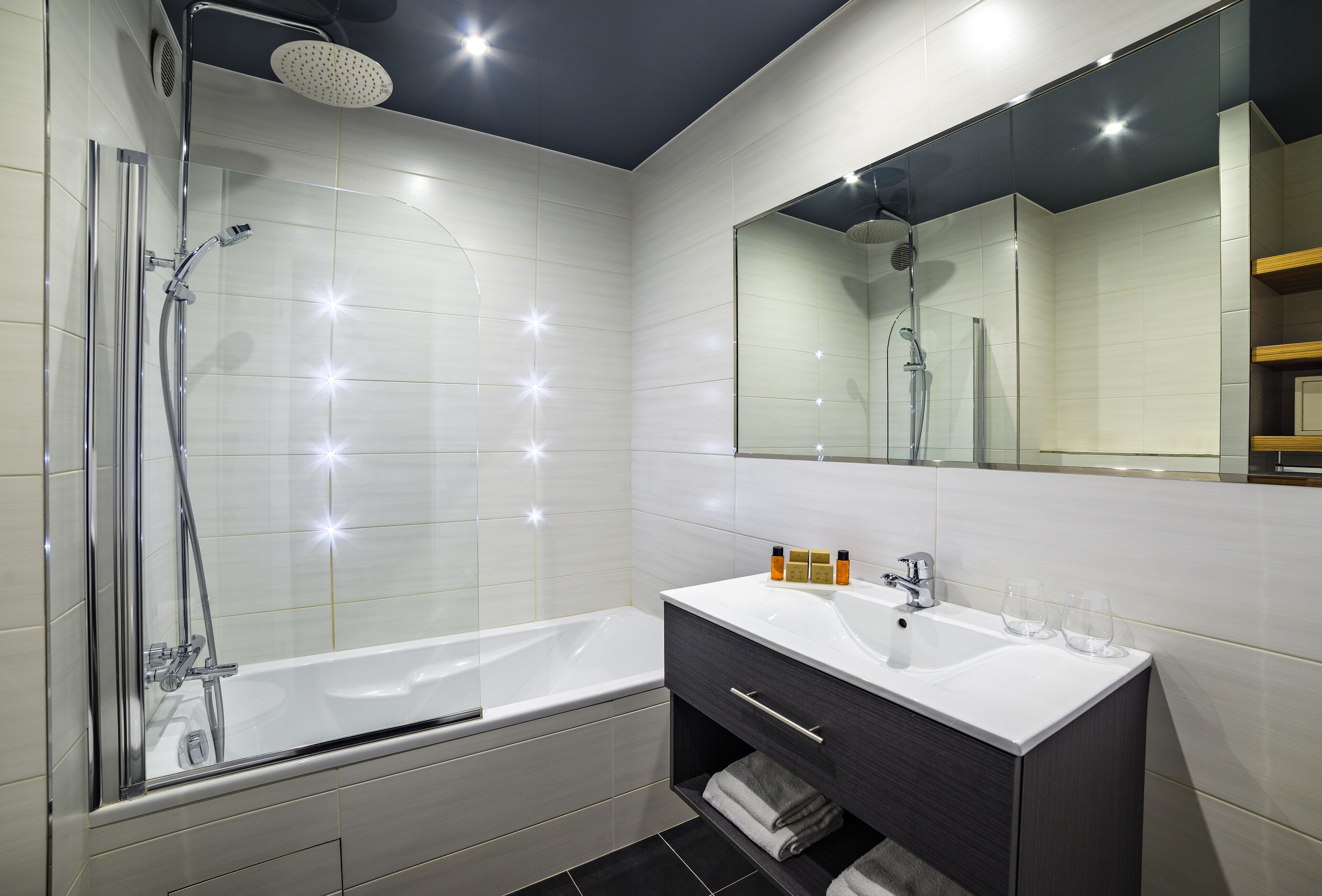 A modern bathroom with a glass-enclosed shower, a white bathtub, and a vanity with a mirror.