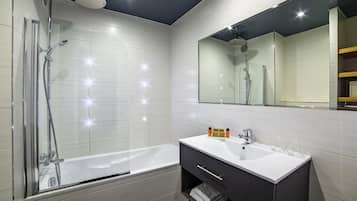A modern bathroom with a glass-enclosed shower, a white bathtub, and a vanity with a mirror.