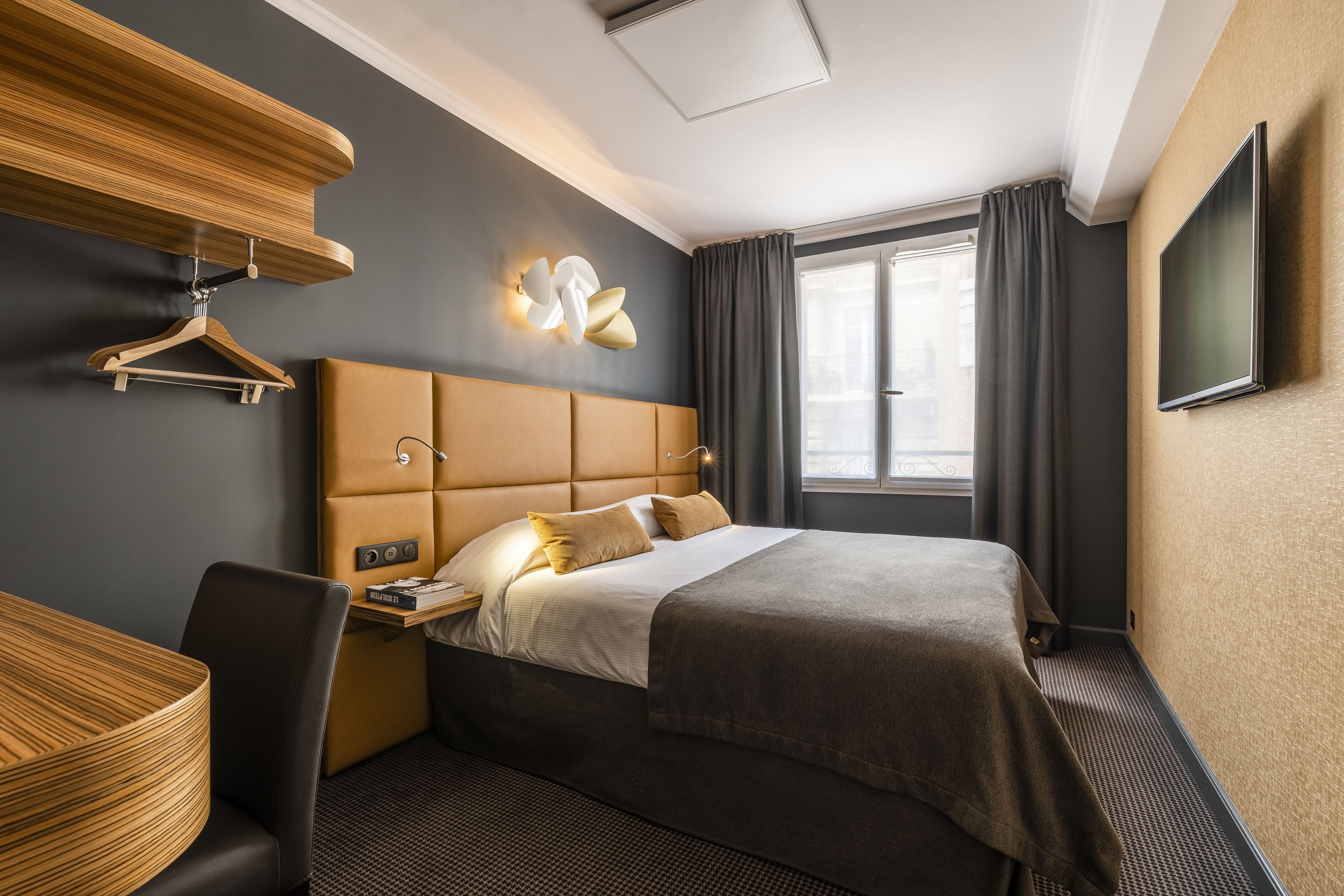 A modern hotel room with a large bed, a bedside table, a lamp, a TV, and a window with curtains.