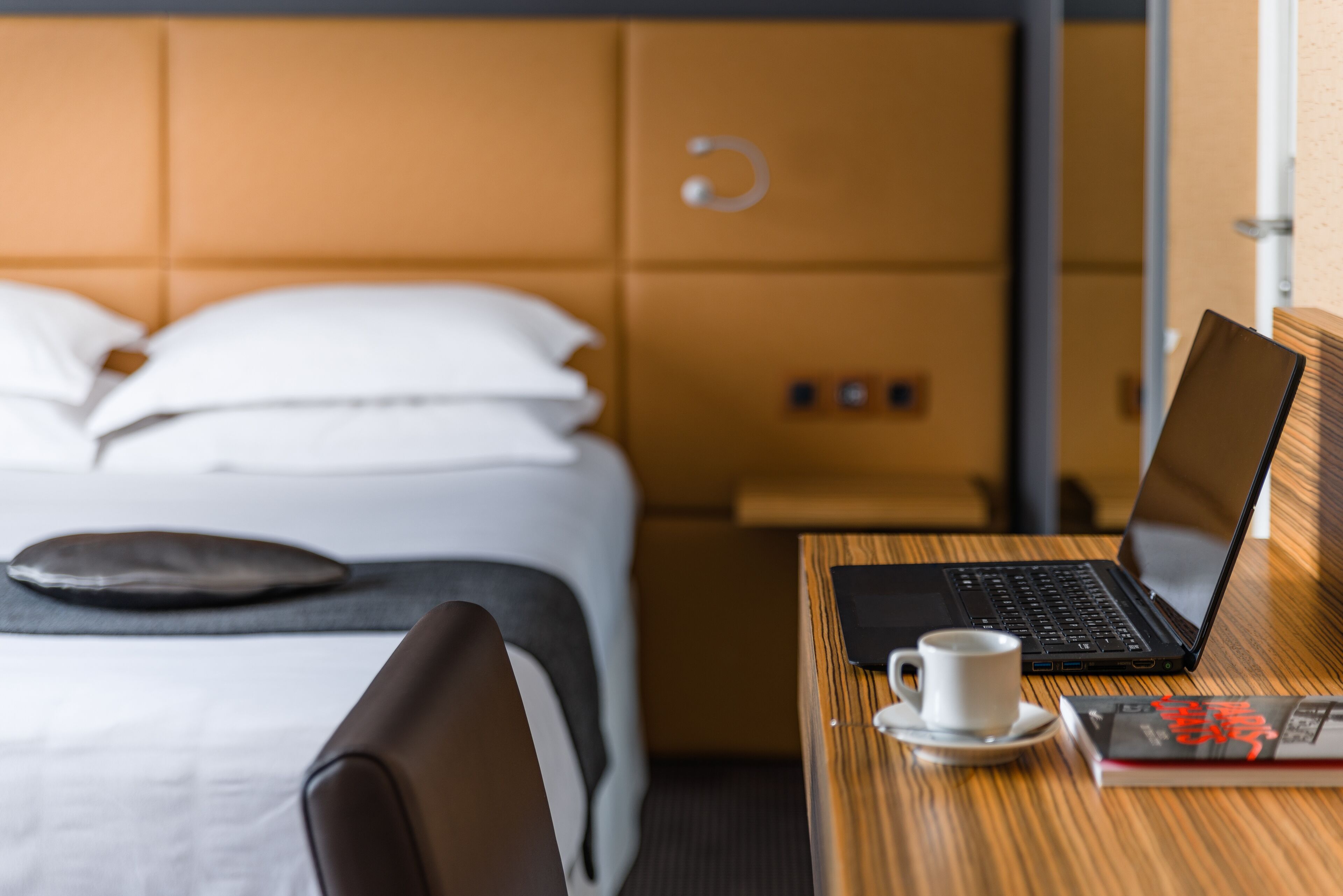 Una habitación de hotel con una cama, un ordenador portátil sobre una mesa de madera, una taza de café y un libro.