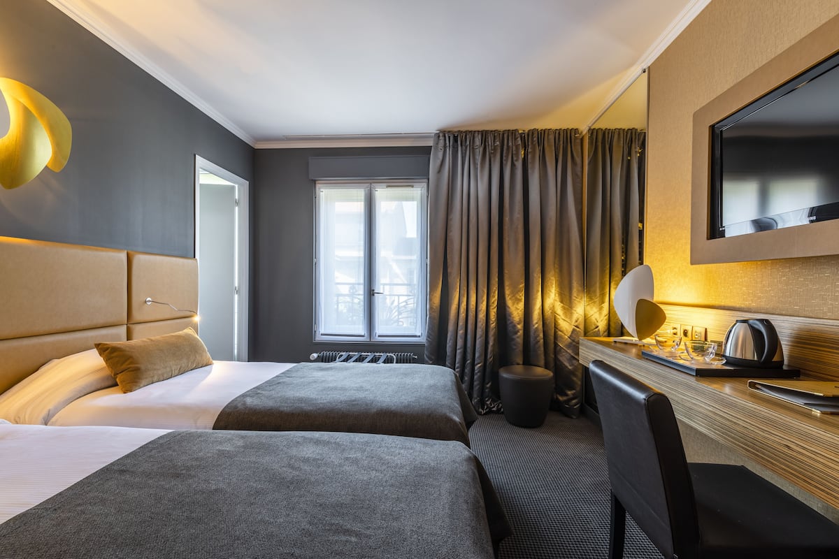 A hotel room with two beds, a desk with a mirror, a flat-screen TV, and a window with curtains.