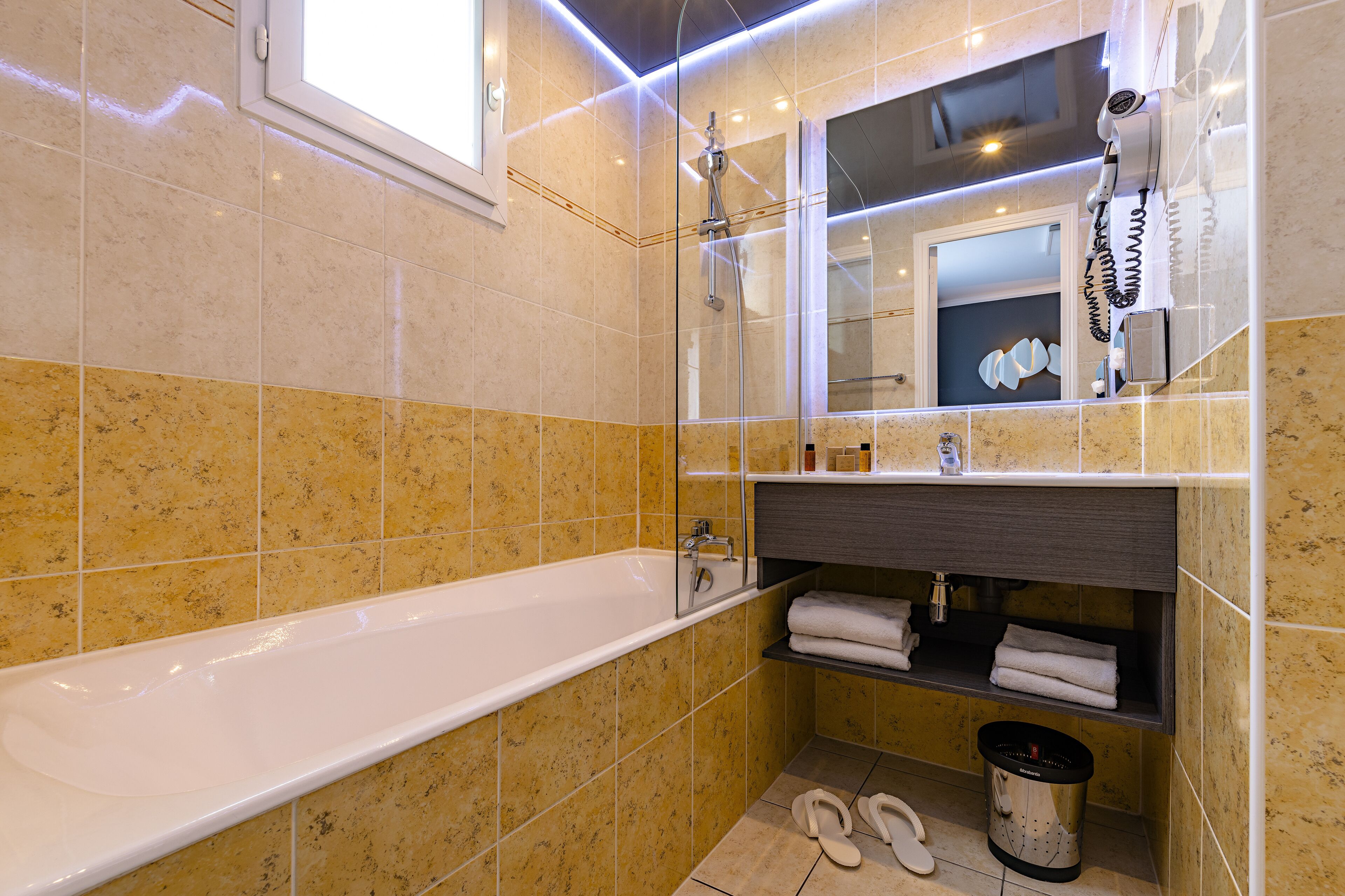 A modern bathroom with a bathtub, a shower, a vanity with a mirror, and a hairdryer mounted on the wall.
