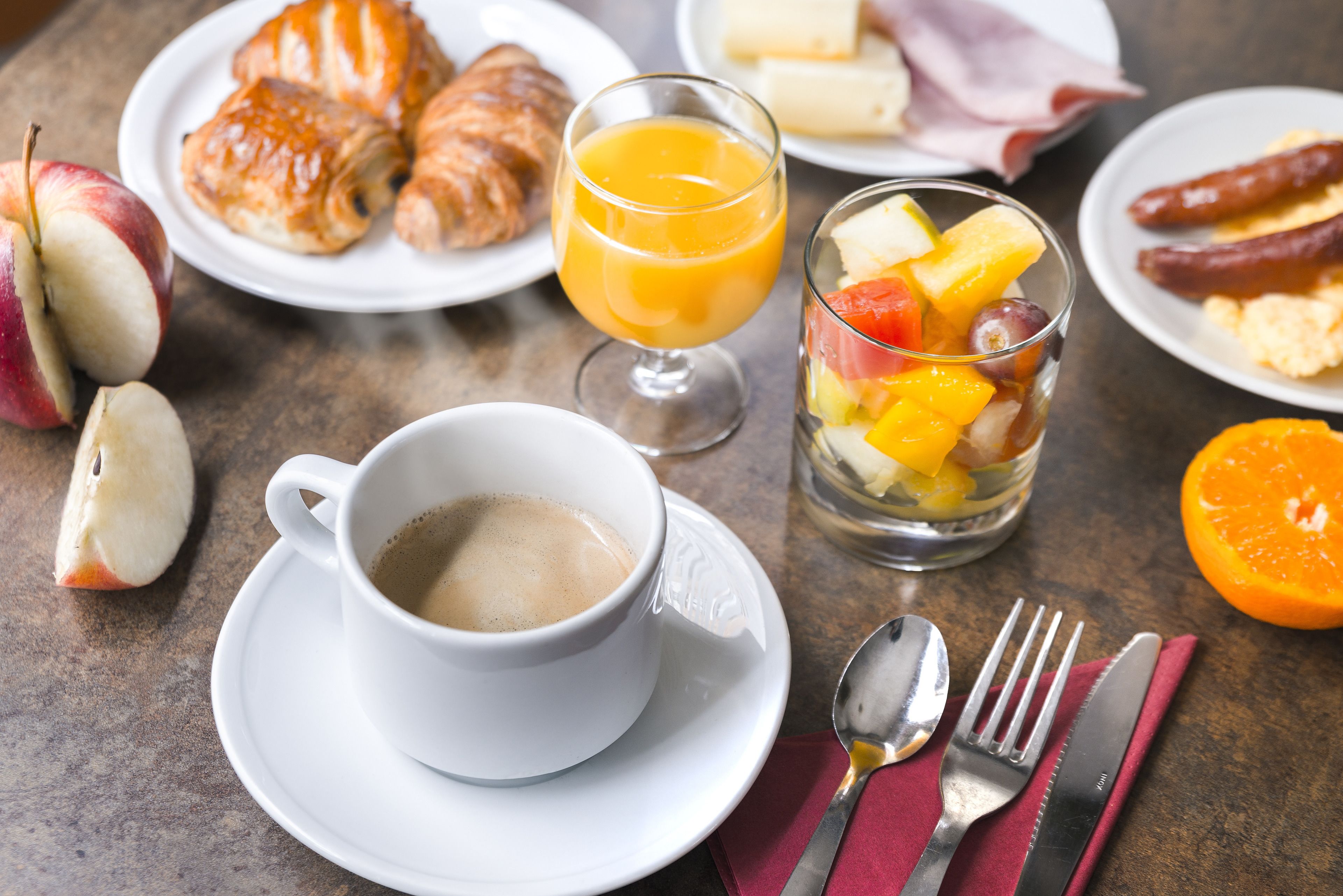 Une table dressée pour le petit-déjeuner, avec des croissants, des fruits, du jus d’orange et du café.