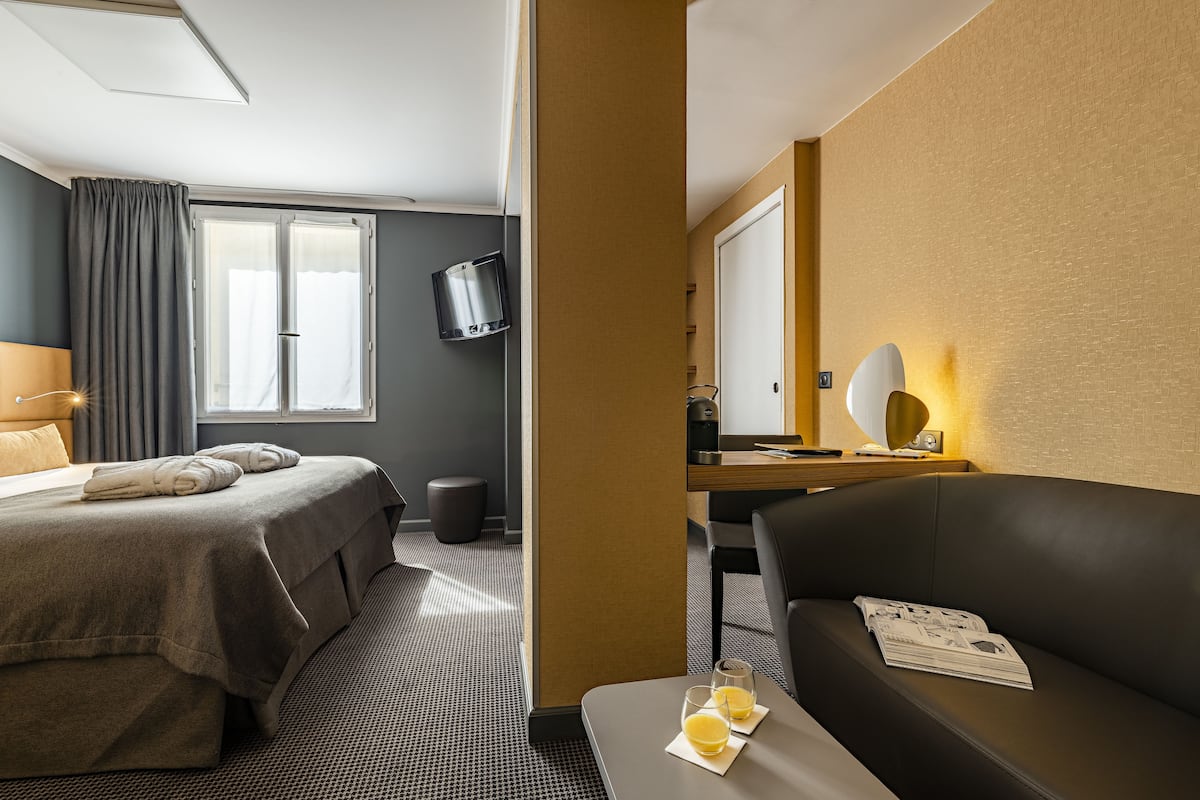 A hotel room with a bed, a sofa, a desk with a lamp, and a TV.