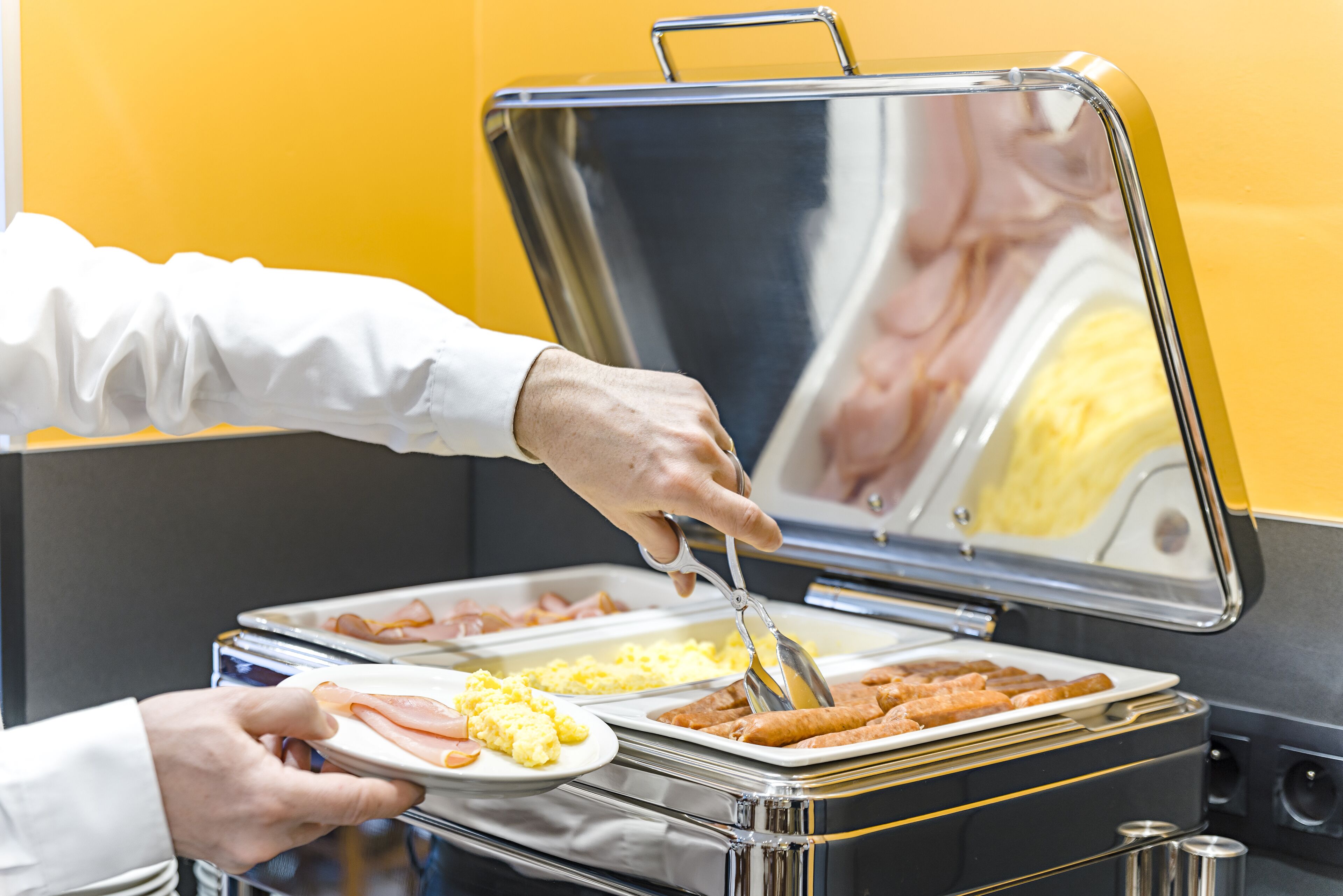 A buffet setup with various food items and a person serving food.