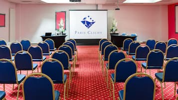 A conference room with rows of blue chairs, a red carpet, and a screen displaying the Paris Clichy logo.